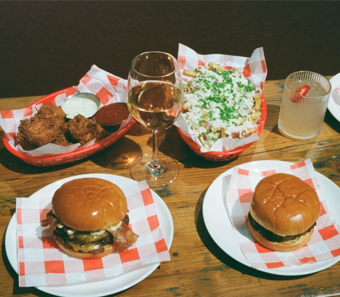 smash burgers, chicken tenders, wine and picante on a table with loaded fries